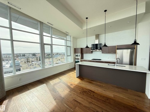 Open concept living area featuring large windows with city views, hardwood flooring, and a modern kitchen with a large island, stainless steel appliances, and pendant lighting - 710 2504 109 Street, Edmonton, AB - Indoor Photo Showing Kitchen With Upgraded Kitchen