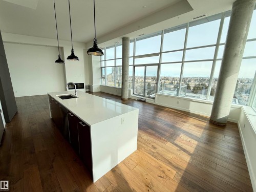 Modern open-concept living space with hardwood floors, floor-to-ceiling windows offering extensive views, and a kitchen island with a sink and pendant lighting - 710 2504 109 Street, Edmonton, AB - Indoor