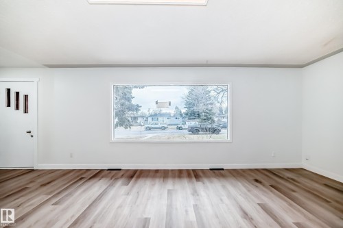 This bright room features a wide window, light-toned flooring, and a white entrance door with decorative vertical panels - 9126 152 St, Edmonton, AB - Indoor Photo Showing Other Room