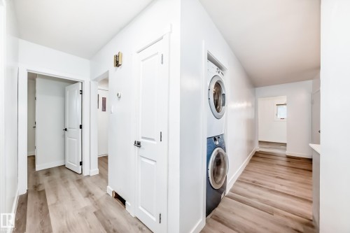 Hallway featuring light-toned flooring and white walls, with a stacked washer and dryer unit - 9126 152 St, Edmonton, AB - Indoor Photo Showing Laundry Room