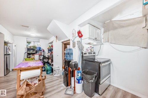 The property features an electric range with an overhead cabinet, a refrigerator, and light wood-style flooring - 9126 152 St, Edmonton, AB - Indoor Photo Showing Laundry Room