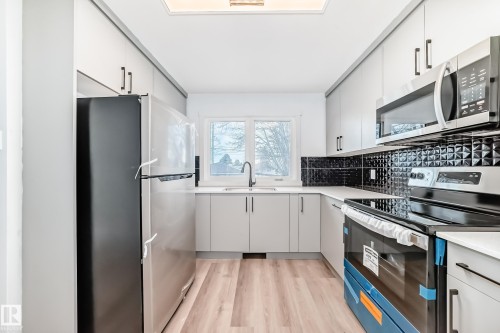 The kitchen features light-colored cabinetry, a black textured tile backsplash, and light wood-style flooring - 9126 152 St, Edmonton, AB - Indoor Photo Showing Kitchen With Upgraded Kitchen