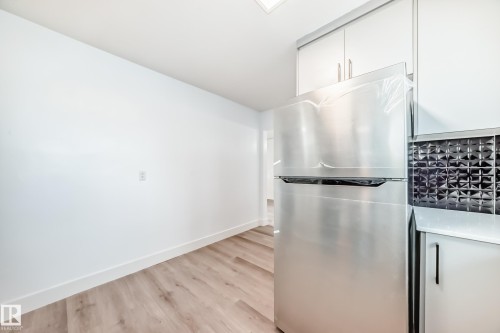 Kitchen area featuring a stainless steel refrigerator, white cabinetry, and a textured dark tile backsplash - 9126 152 St, Edmonton, AB - Indoor