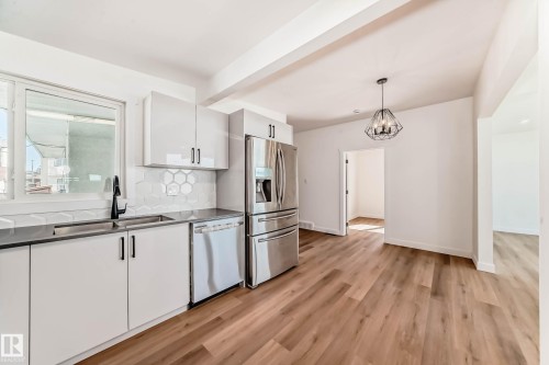 The kitchen features light-colored cabinetry, stainless steel appliances, a window above the sink, and light wood-style flooring - 7220 152A Ave, Edmonton, AB - Indoor Photo Showing Kitchen