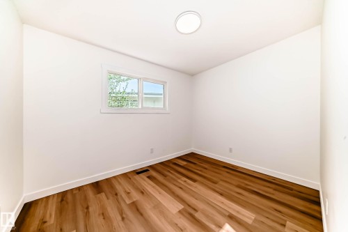 This room features light-colored walls, wood-style flooring, a window, and a ceiling light fixture - 7220 152A Ave, Edmonton, AB - Indoor Photo Showing Other Room