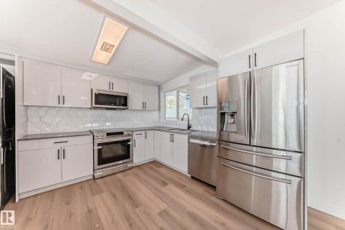The kitchen features L-shaped white cabinetry with dark hardware, stainless steel appliances, and wood-style flooring - 7220 152A Ave, Edmonton, AB - Indoor Photo Showing Kitchen With Upgraded Kitchen