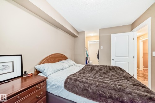 The bedroom features neutral-toned walls, a wooden headboard, and a classic dresser - 116 5810 Mullen Place, Edmonton, AB - Indoor Photo Showing Bedroom