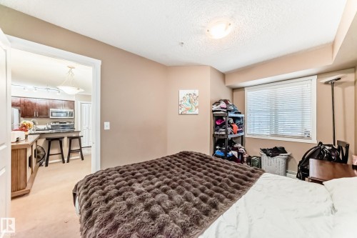 This room features a window with blinds, light-colored walls, and a ceiling light fixture - 116 5810 Mullen Place, Edmonton, AB - Indoor Photo Showing Bedroom