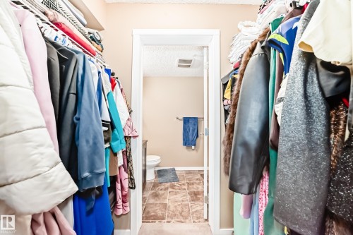 Walk-in closet with ample hanging space, providing convenient access to an en-suite with a toilet and tiled flooring - 116 5810 Mullen Place, Edmonton, AB - Indoor With Storage