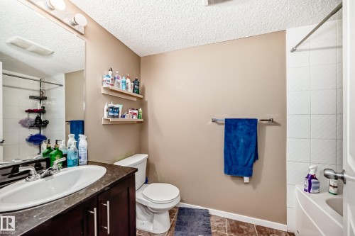Bathroom featuring a vanity with an integrated sink, a toilet, and a bathtub with a shower - 116 5810 Mullen Place, Edmonton, AB - Indoor Photo Showing Bathroom