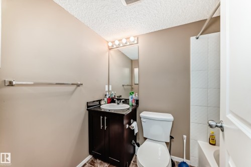 The bathroom features a vanity with a dark wood cabinet, a white oval sink, and a mirror with a four-bulb light fixture above it - 116 5810 Mullen Place, Edmonton, AB - Indoor Photo Showing Bathroom