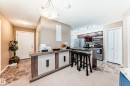 The property features a kitchen with dark cabinetry, stainless steel appliances, and a kitchen island with seating - 116 5810 Mullen Place, Edmonton, AB  - Indoor Photo Showing Kitchen 