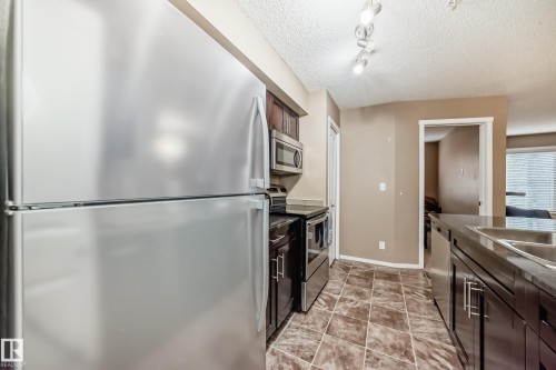 The kitchen features a stainless steel refrigerator, microwave, and stove - 116 5810 Mullen Place, Edmonton, AB - Indoor Photo Showing Kitchen