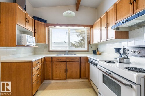 U-shaped kitchen featuring wood cabinetry with black hardware, white countertops, and a white tile backsplash - 13437 118 Street, Edmonton, AB - Indoor Photo Showing Kitchen With Double Sink