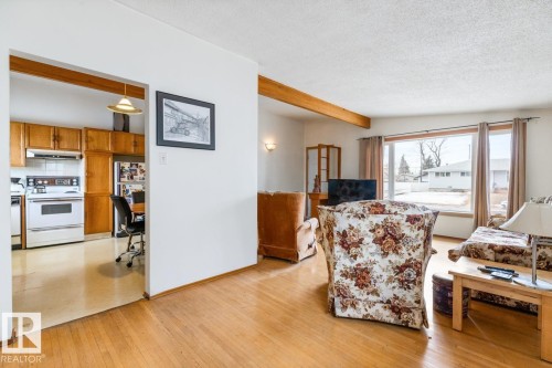 Bright living space featuring wood-finish flooring, exposed ceiling beams, and a large picture window - 13437 118 Street, Edmonton, AB - Indoor Photo Showing Other Room