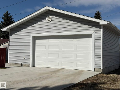 Detached garage featuring light grey horizontal siding, a white panel garage door, a white gable vent, white trim, and a concrete driveway approach - 13437 118 Street, Edmonton, AB - Outdoor With Exterior