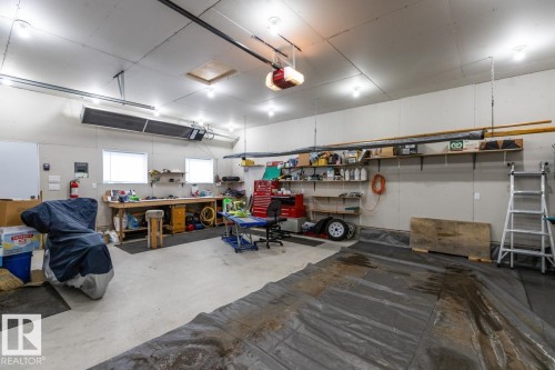 Spacious garage interior featuring high ceilings, ample overhead lighting, two large windows, extensive built-in shelving, and a robust workbench - 13437 118 Street, Edmonton, AB - Indoor Photo Showing Garage