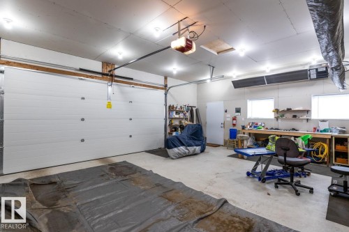 Spacious garage featuring a large white overhead door, concrete flooring, overhead lighting, two windows, and built-in workbench cabinetry - 13437 118 Street, Edmonton, AB - Indoor Photo Showing Garage