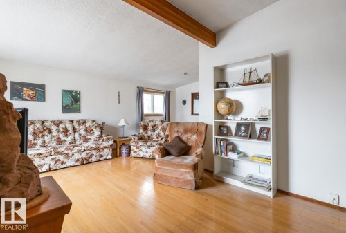 Open living area with a prominent exposed wood ceiling beam and wood-finish flooring, - 13437 118 Street, Edmonton, AB - Indoor Photo Showing Living Room