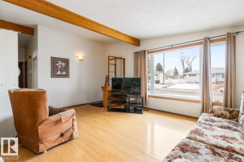 Expansive living area featuring light wood-finish flooring, exposed ceiling beams, and a large picture window - 13437 118 Street, Edmonton, AB - Indoor