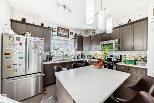 The kitchen features a stainless steel refrigerator, dark wood cabinetry, white countertops, and a white subway tile backsplash - 8204 224 Nw, Edmonton, AB - Indoor Photo Showing Kitchen With Stainless Steel Kitchen With Double Sink