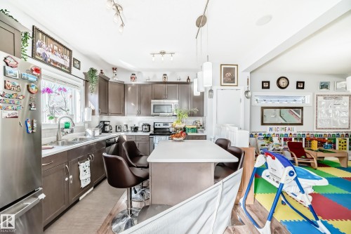 The kitchen features dark wood cabinetry, a stainless steel refrigerator, and a kitchen island with a light-colored countertop - 8204 224 Nw, Edmonton, AB - Indoor Photo Showing Kitchen