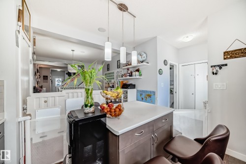 The kitchen features a functional island with a light-colored countertop and dark cabinetry, illuminated by three pendant lights - 8204 224 Nw, Edmonton, AB - Indoor Photo Showing Other Room