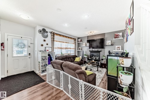 Inviting living area featuring wood-style flooring, a decorative fireplace, and a large window with blinds - 8204 224 Nw, Edmonton, AB - Indoor With Fireplace