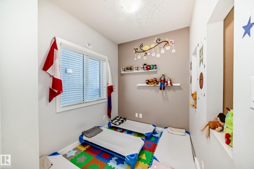 A bright room with neutral wall colors and a window providing natural light, featuring decorative wall shelving and an overhead light fixture - 8204 224 Nw, Edmonton, AB - Indoor