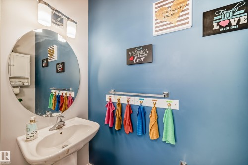Bathroom featuring a pedestal sink with a chrome faucet, a large circular mirror, and a wall-mounted light fixture - 8204 224 Nw, Edmonton, AB - Indoor Photo Showing Bathroom