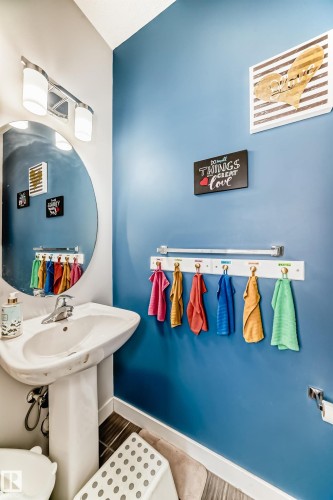 Bathroom featuring a pedestal sink, a circular mirror, and a wall-mounted light fixture - 8204 224 Nw, Edmonton, AB - Indoor Photo Showing Bathroom