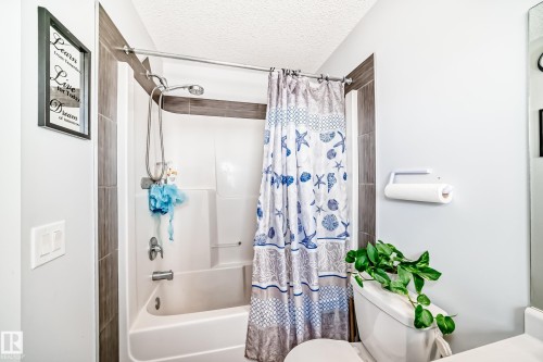 The bathroom features a shower and bathtub combination with tiled surround, a toilet, and a toilet paper holder - 8204 224 Nw, Edmonton, AB - Indoor Photo Showing Bathroom