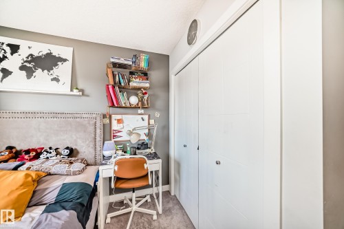 This room features a neutral color palette, a bed with a studded headboard, and a desk area with shelving - 8204 224 Nw, Edmonton, AB - Indoor
