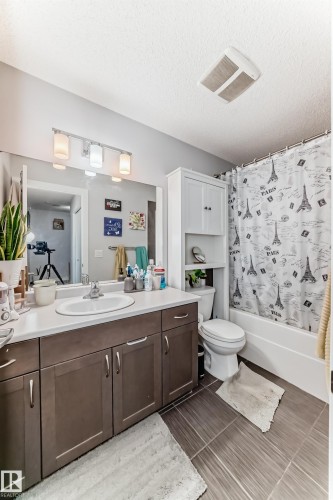 The bathroom features a vanity with a white countertop and a single basin sink, a toilet, and a bathtub with a shower curtain - 8204 224 Nw, Edmonton, AB - Indoor Photo Showing Bathroom
