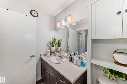Bathroom featuring a vanity with a white countertop and dark cabinetry, a white sink with a chrome faucet, and a wall-mounted mirror with overhead lighting - 8204 224 Nw, Edmonton, AB - Indoor Photo Showing Bathroom