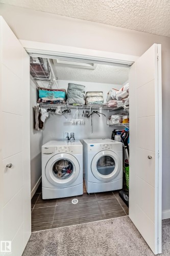 Dedicated laundry area featuring a white front-loading washer and dryer, with tiled flooring and wire shelving for storage - 8204 224 Nw, Edmonton, AB - Indoor Photo Showing Laundry Room