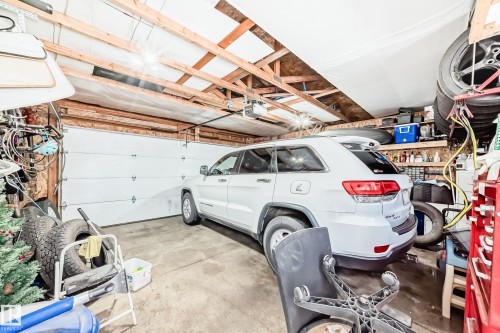 The property features a garage with a roll-up door, exposed ceiling joists, and concrete flooring - 8204 224 Nw, Edmonton, AB - Indoor Photo Showing Garage