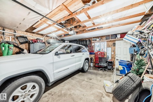 Spacious garage featuring exposed wood beams, concrete flooring, and a white door - 8204 224 Nw, Edmonton, AB - Indoor Photo Showing Garage