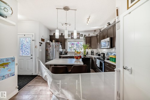 The kitchen features dark wood cabinetry, stainless steel appliances, and a central island with seating - 8204 224 Nw, Edmonton, AB - Indoor Photo Showing Kitchen With Upgraded Kitchen