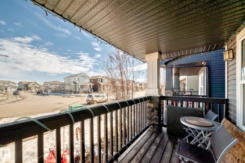 This property features an inviting covered porch with a wooden floor, a stone column, and a black wooden railing - 8204 224 Nw, Edmonton, AB - Outdoor With Deck Patio Veranda With Exterior
