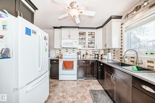 Dual tone kitchen featuring white appliances, glass insert cabinets, a ceiling fan, tasteful backsplash, and light countertops - 3634 113 Avenue, Edmonton, AB - Indoor Photo Showing Kitchen