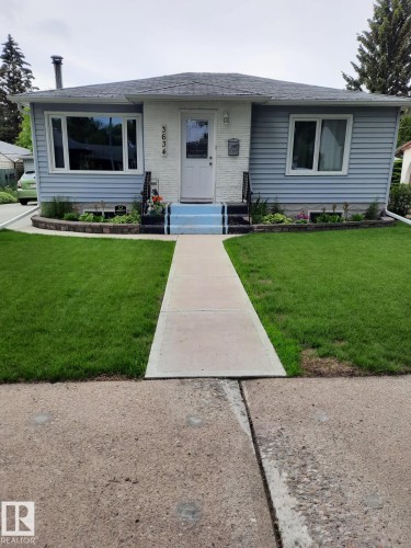 The property features light blue siding, a white front door, and a well-maintained front lawn with a concrete pathway leading to the entrance - 3634 113 Avenue, Edmonton, AB - Outdoor