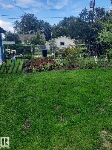The property features a well-maintained lawn and a garden area with various plantings, enclosed by a black metal fence - 3634 113 Avenue, Edmonton, AB - Outdoor