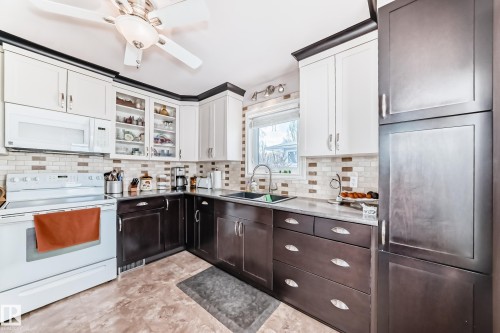 Dual tone kitchen featuring white appliances, glass insert cabinets, two tone cabinets, ceiling fan, and tasteful backsplash - 3634 113 Avenue, Edmonton, AB - Indoor Photo Showing Kitchen With Double Sink