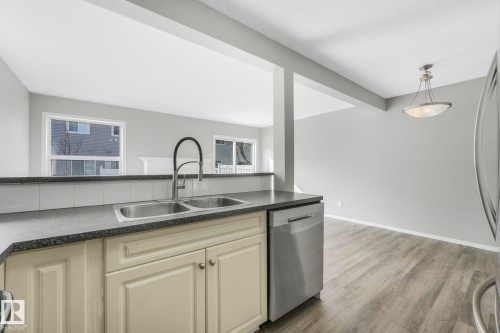 The kitchen features a double basin sink with a high-arc faucet, light-colored cabinetry, a dark countertop, and a stainless steel dishwasher - 123 230 Edwards Drive, Edmonton, AB - Indoor Photo Showing Kitchen With Double Sink
