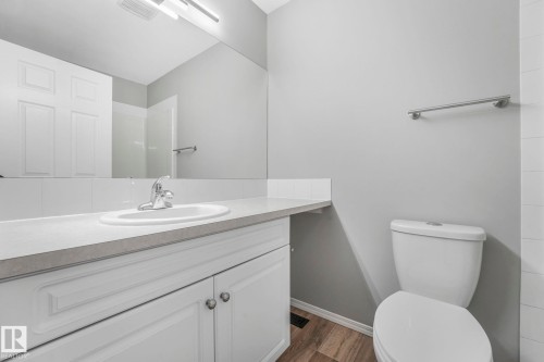 Bathroom featuring a white vanity with a light-colored countertop and an integrated sink, a toilet, and wood-look flooring - 123 230 Edwards Drive, Edmonton, AB - Indoor Photo Showing Bathroom