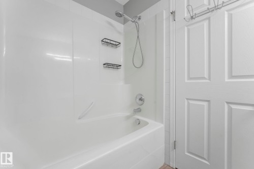 Bathroom featuring a white bathtub with a shower system and two wall-mounted storage racks - 123 230 Edwards Drive, Edmonton, AB - Indoor Photo Showing Bathroom