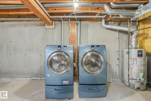 Laundry area featuring concrete walls and floors, exposed ceiling beams, and a water heater - 123 230 Edwards Drive, Edmonton, AB - Indoor Photo Showing Laundry Room