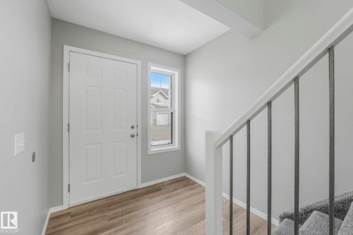Entrance area featuring wood-look flooring, a white paneled door, and a staircase with a white railing and dark balusters - 123 230 Edwards Drive, Edmonton, AB - Indoor Photo Showing Other Room