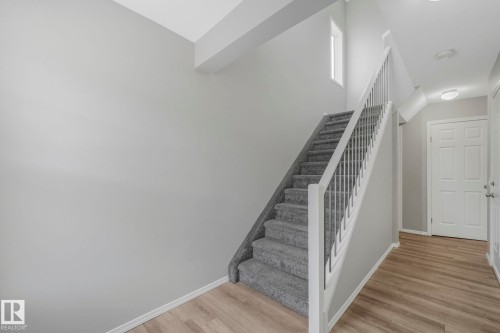 The property features a staircase with carpeted steps and white railings, a front door with white panels, and light wood flooring in the entryway - 123 230 Edwards Drive, Edmonton, AB - Indoor Photo Showing Other Room